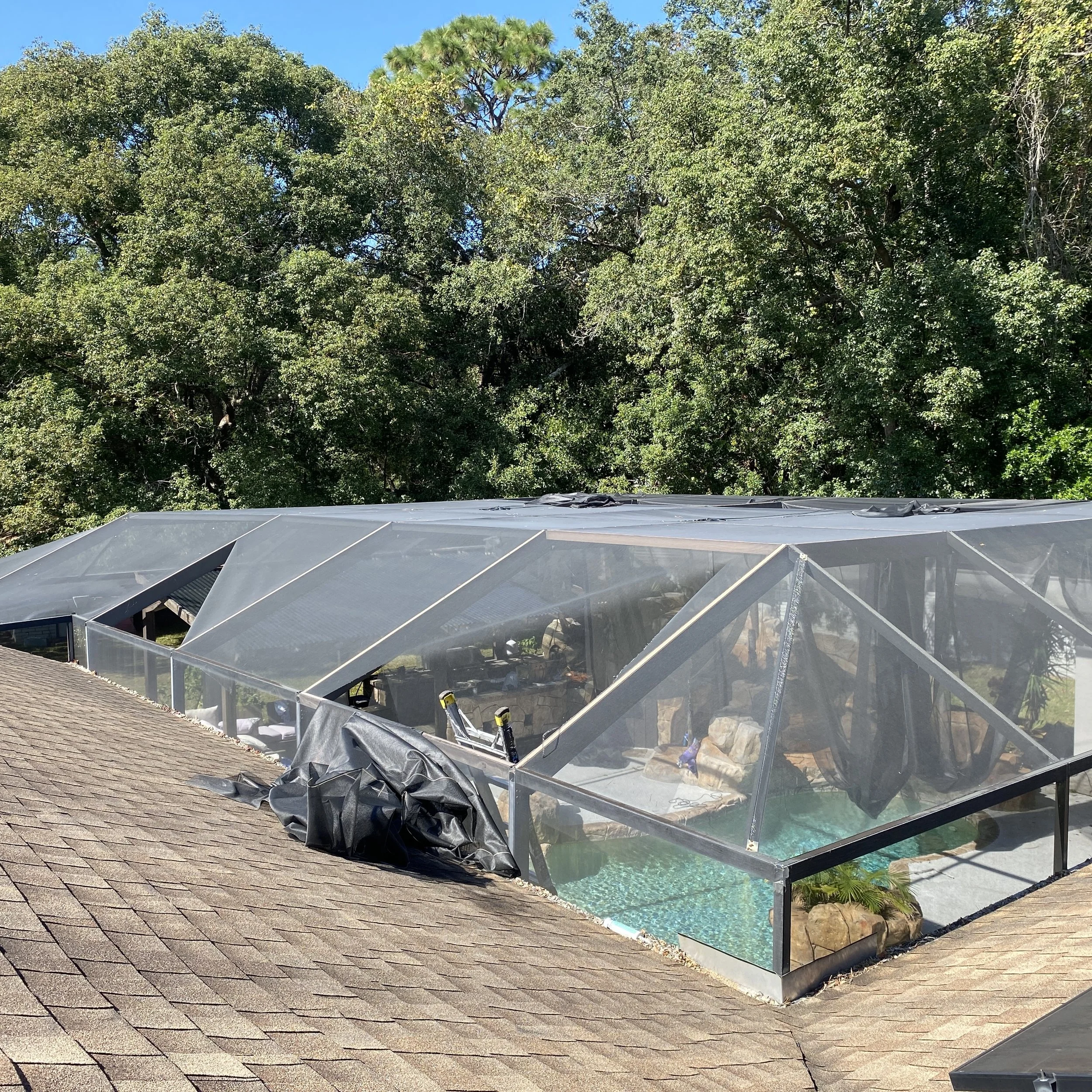 A house with a screened-in pool area covering part of the roof, surrounded by trees, with a blue sky overhead.