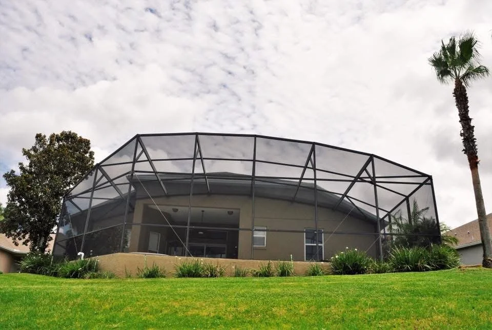 Residential house with a modern screened porch, green lawn, palm tree, and cloudy sky.