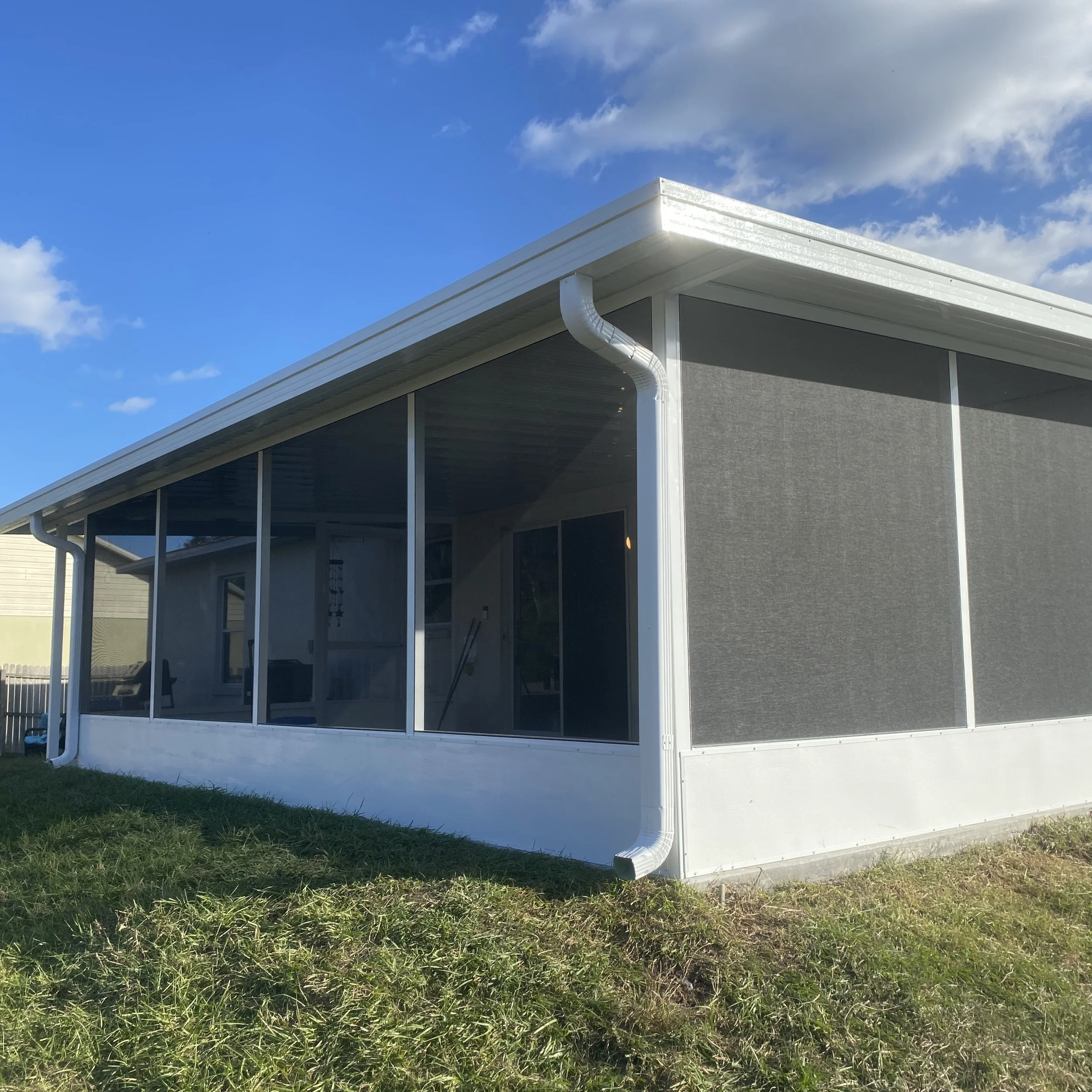 A house with a screened porch, gray walls, a white gutter system, and a clear blue sky with some clouds.