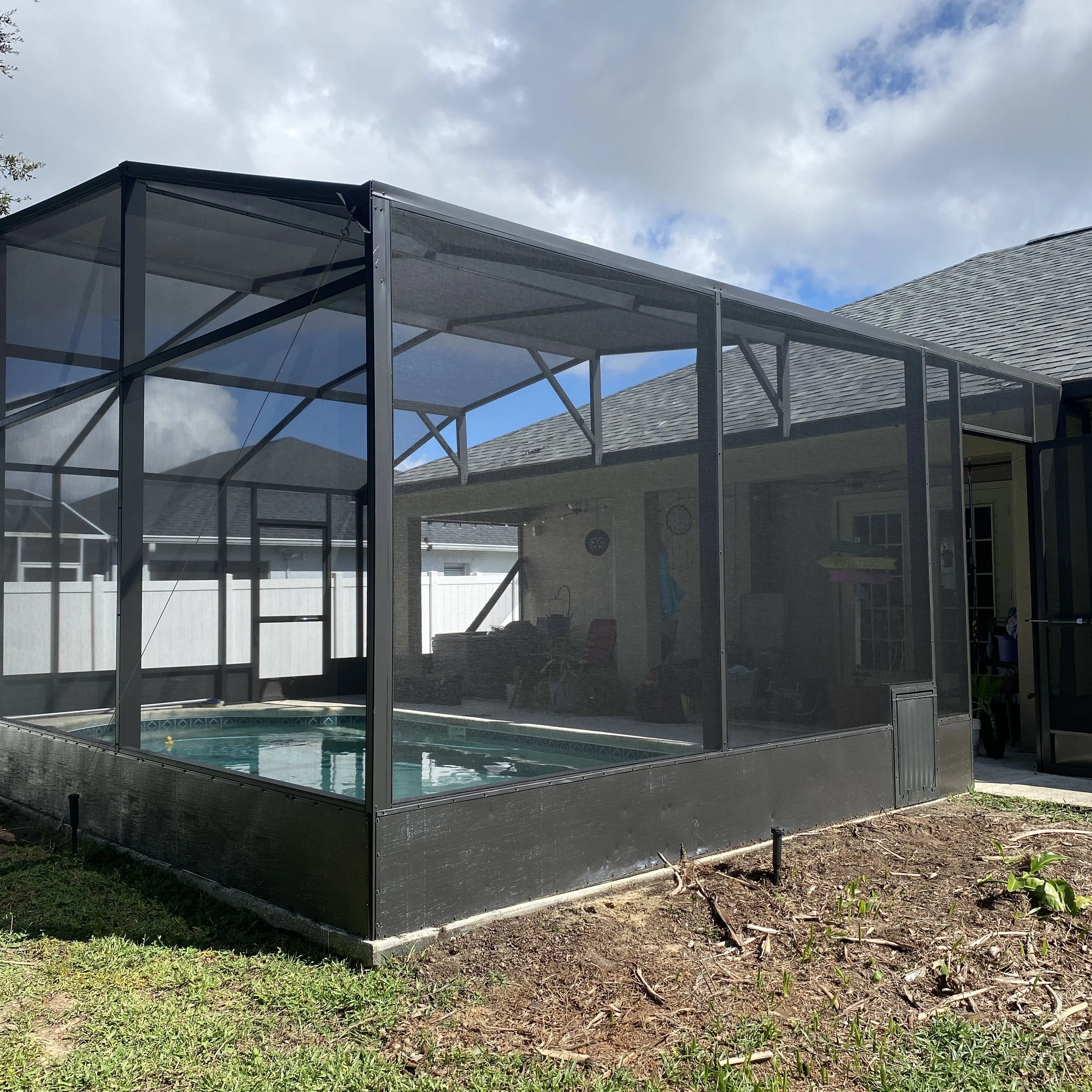 Screened-in pool enclosure with a backyard pool inside, part of a house visible in the background, under a partly cloudy sky.
