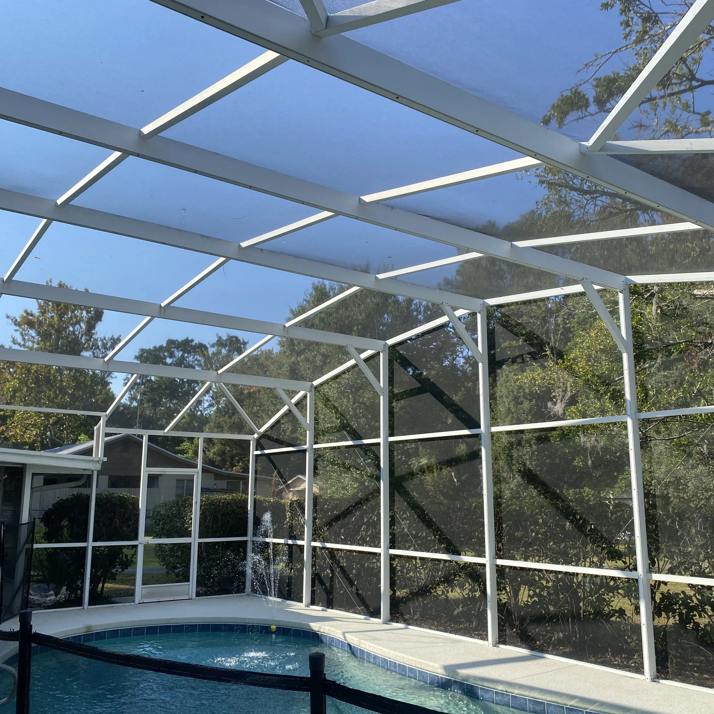 Screened-in backyard pool area with a blue swimming pool, a waterfall feature, and a white metal screen enclosure under a clear blue sky.