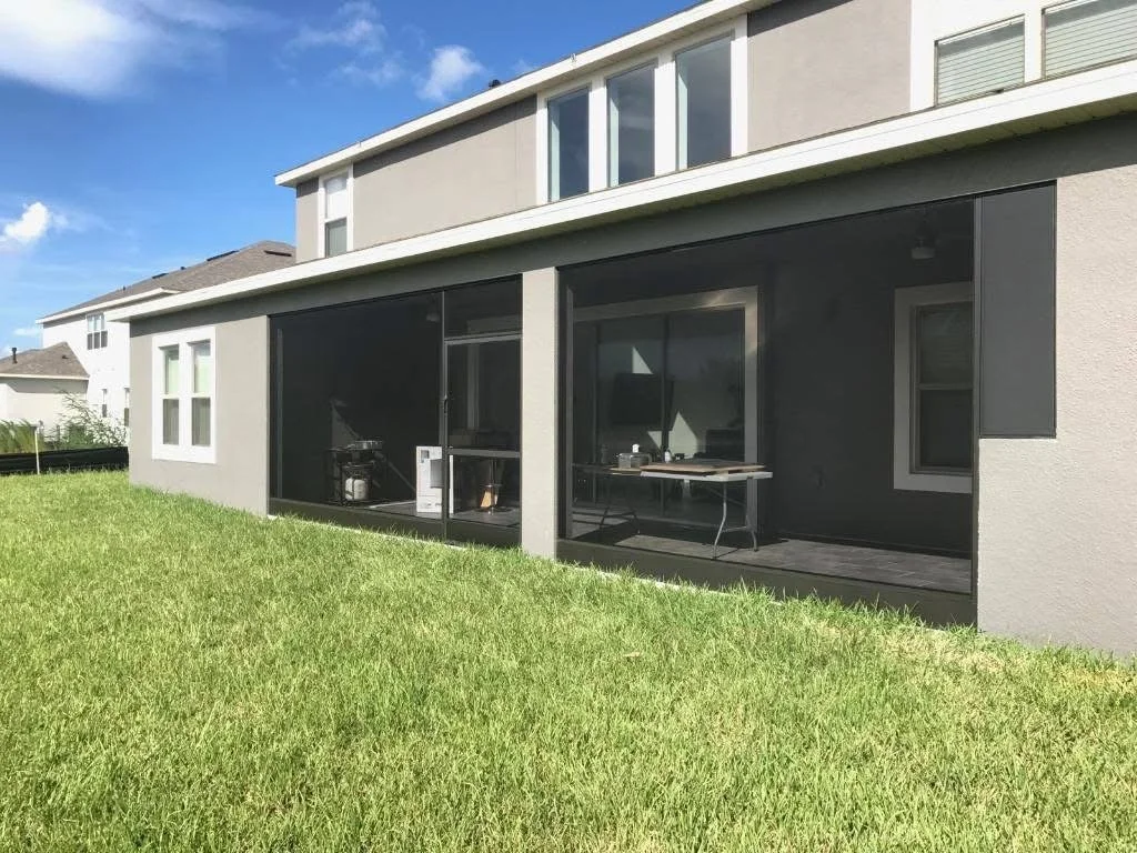 A modern house with a screened-in porch area, a table with some items on it, and a grassy yard in the foreground.