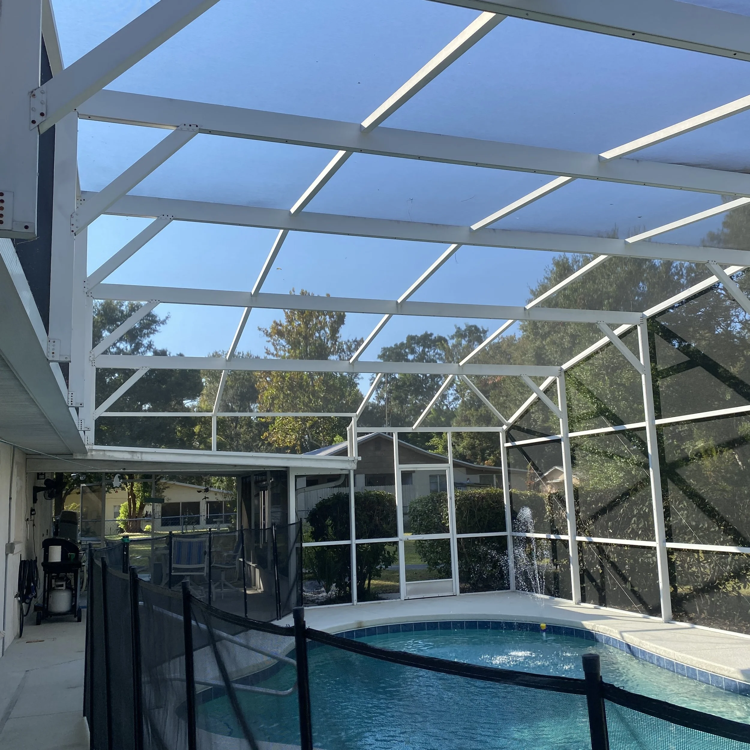 Enclosed backyard swimming pool with a screened roof and surrounding deck, in a suburban neighborhood.