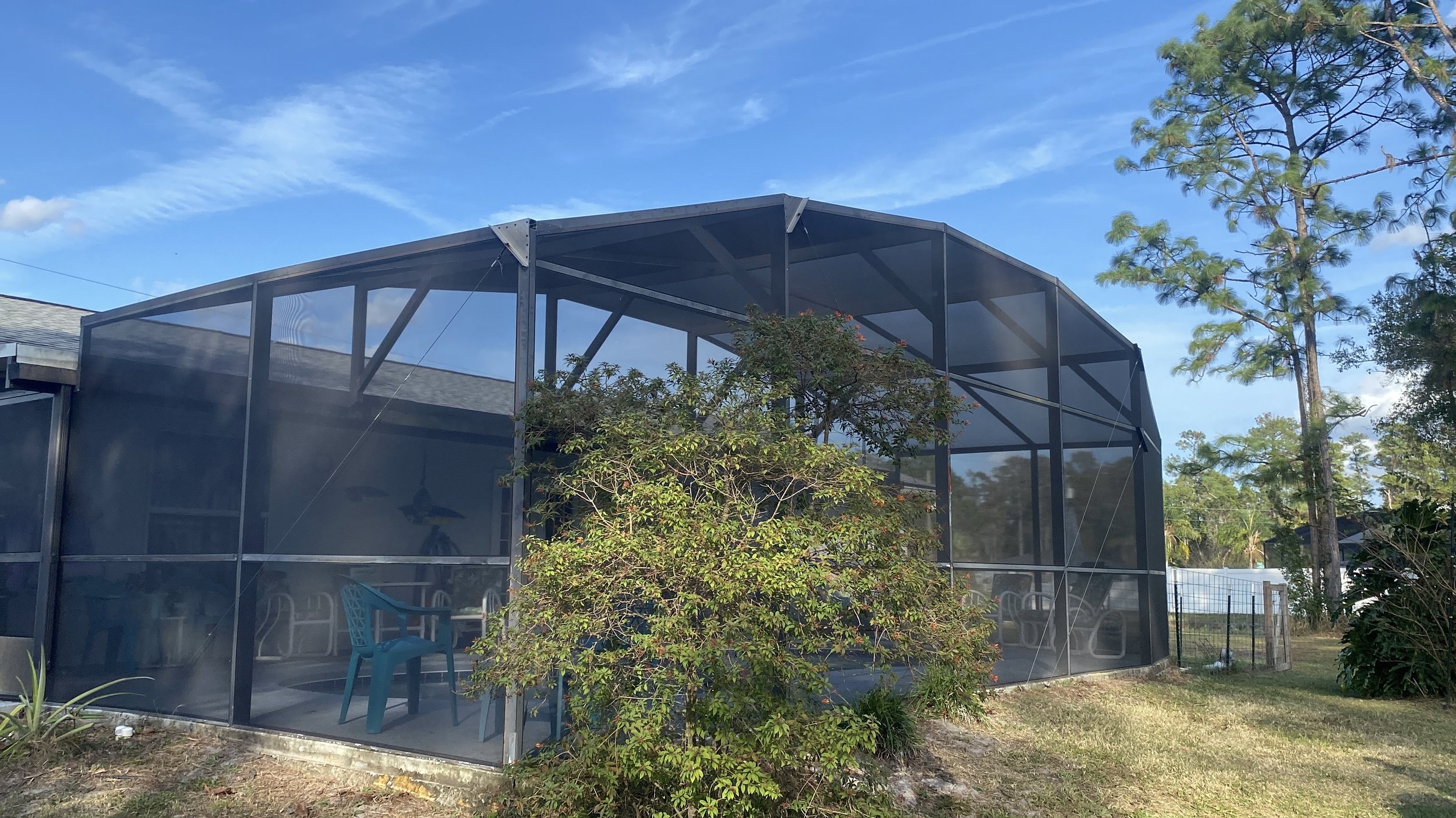 Screened porch with blue chair, outdoor furniture, trees, and a partly cloudy sky.