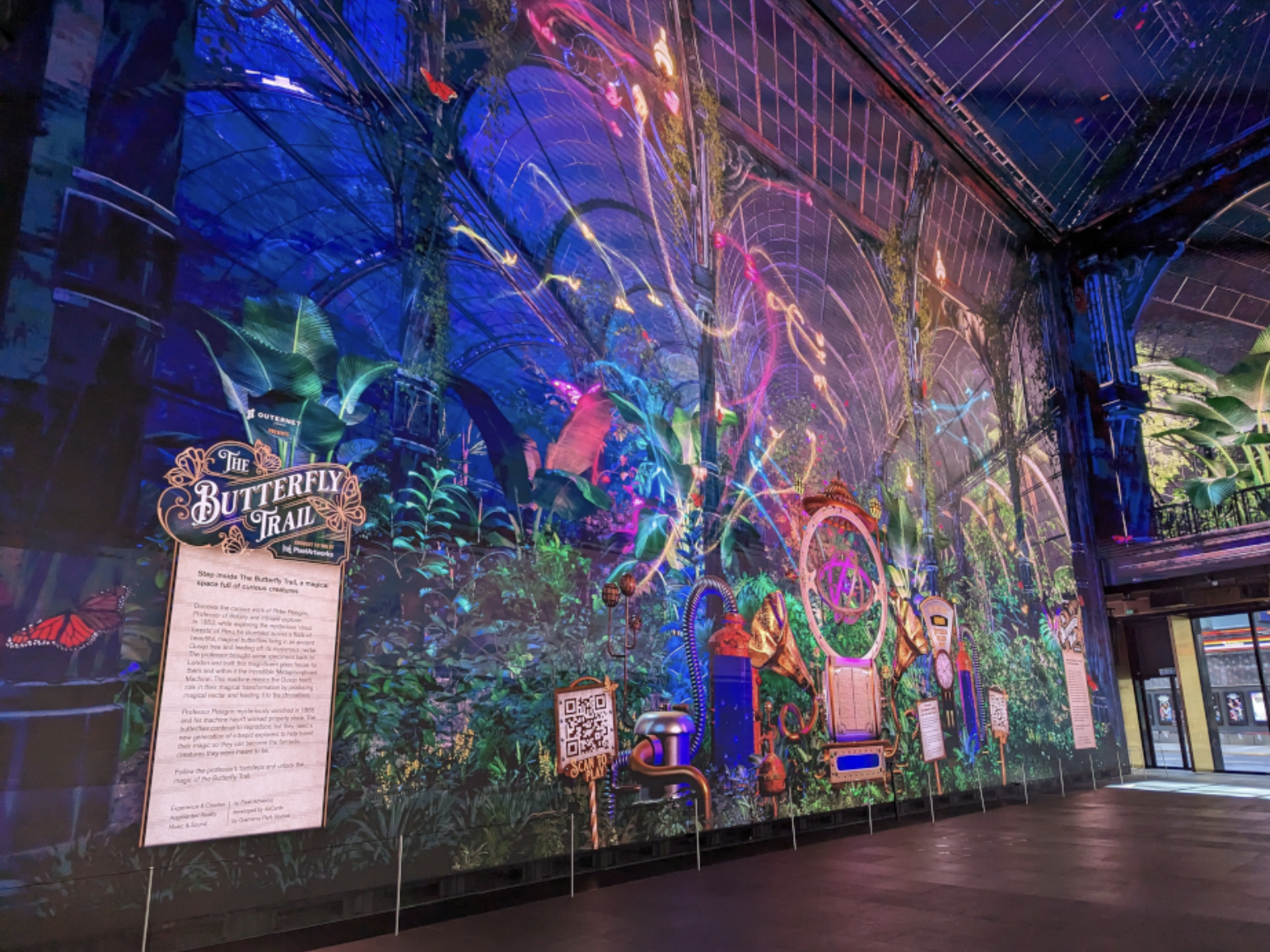 Colorful display at The Butterfly Trail with vibrant neon lights, tropical plants, and informational signs.