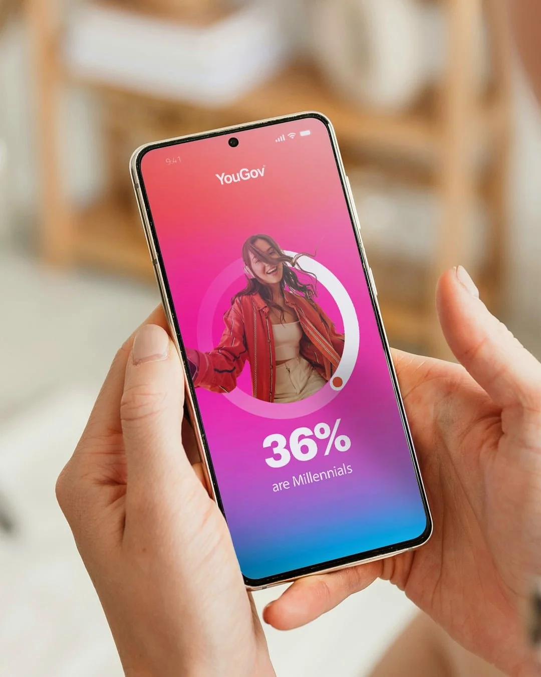 A person holding a smartphone displaying a YouGov poll indicating 36% of millennials, with a vibrant pink background and a smiling young woman in the image.