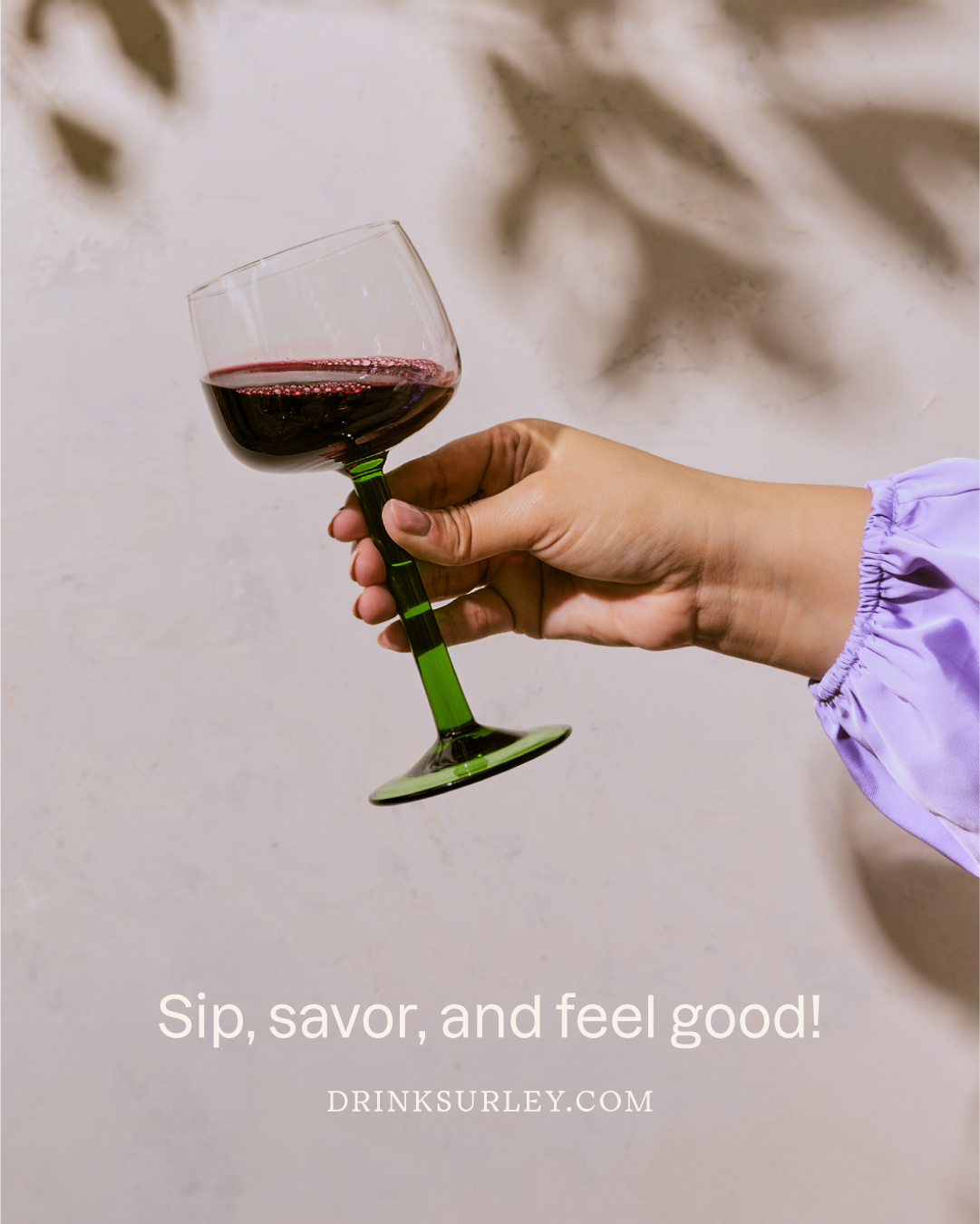 A person holding a glass of red wine with a green stem against a light background with shadows. Text overlay says "Sip, savor, and feel good!" and a website link.
