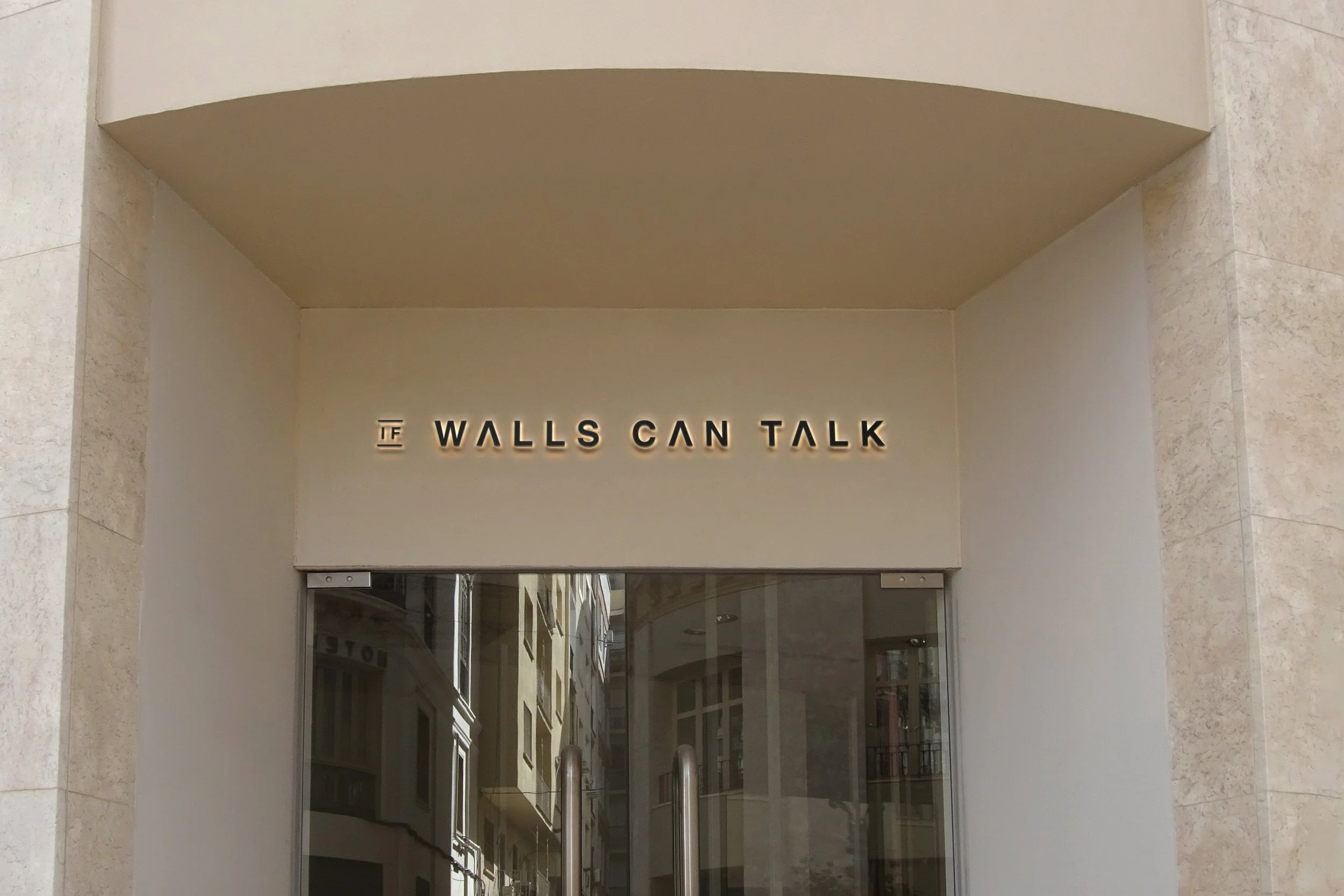 Storefront with a sign that says 'Walls Can Talk' on a beige wall above a glass door.