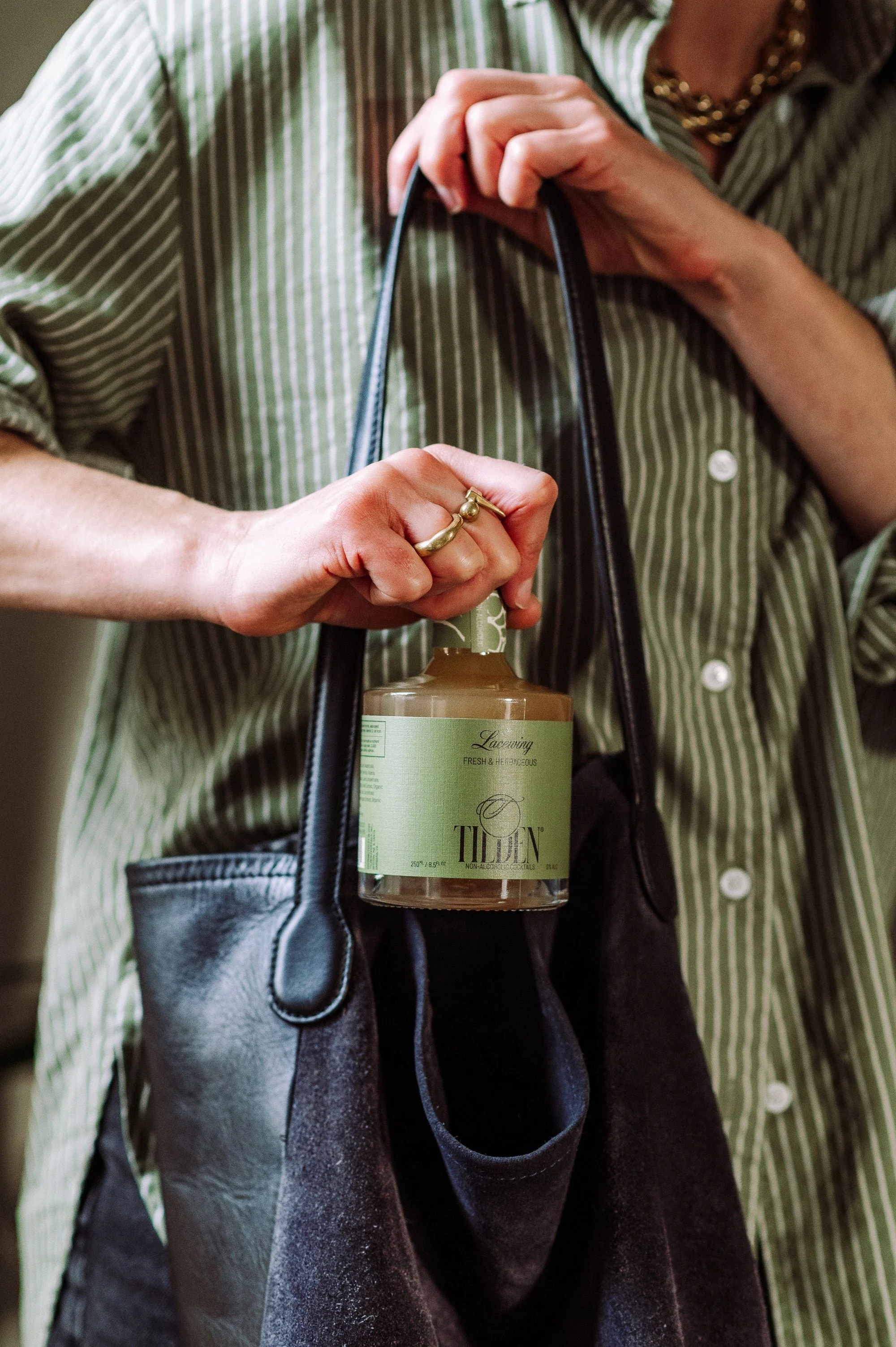 Person holding a black handbag with a jar of Tilden brand sauce or condiment inside.
