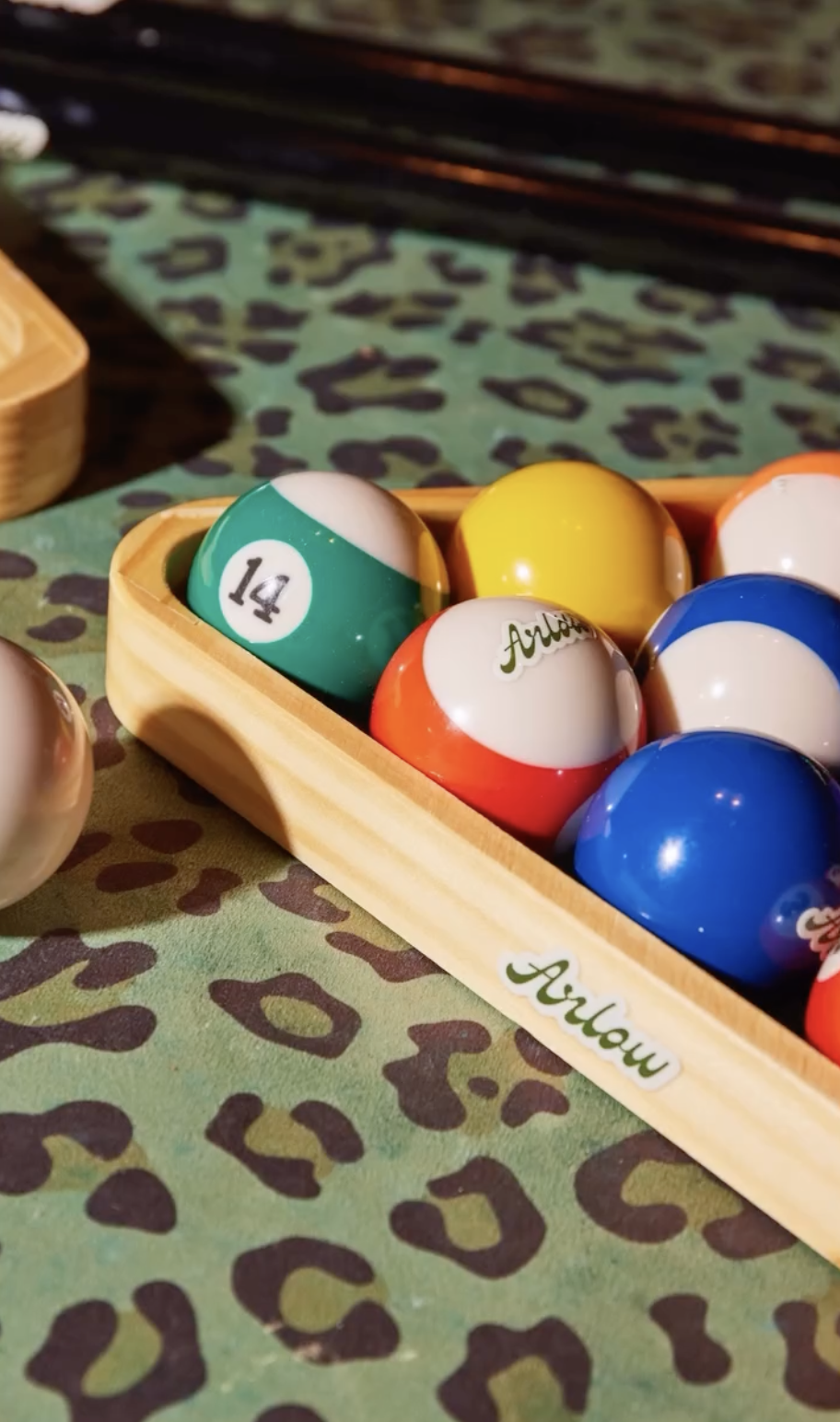 Colorful pool balls in a wooden tray on a patterned green and brown surface.