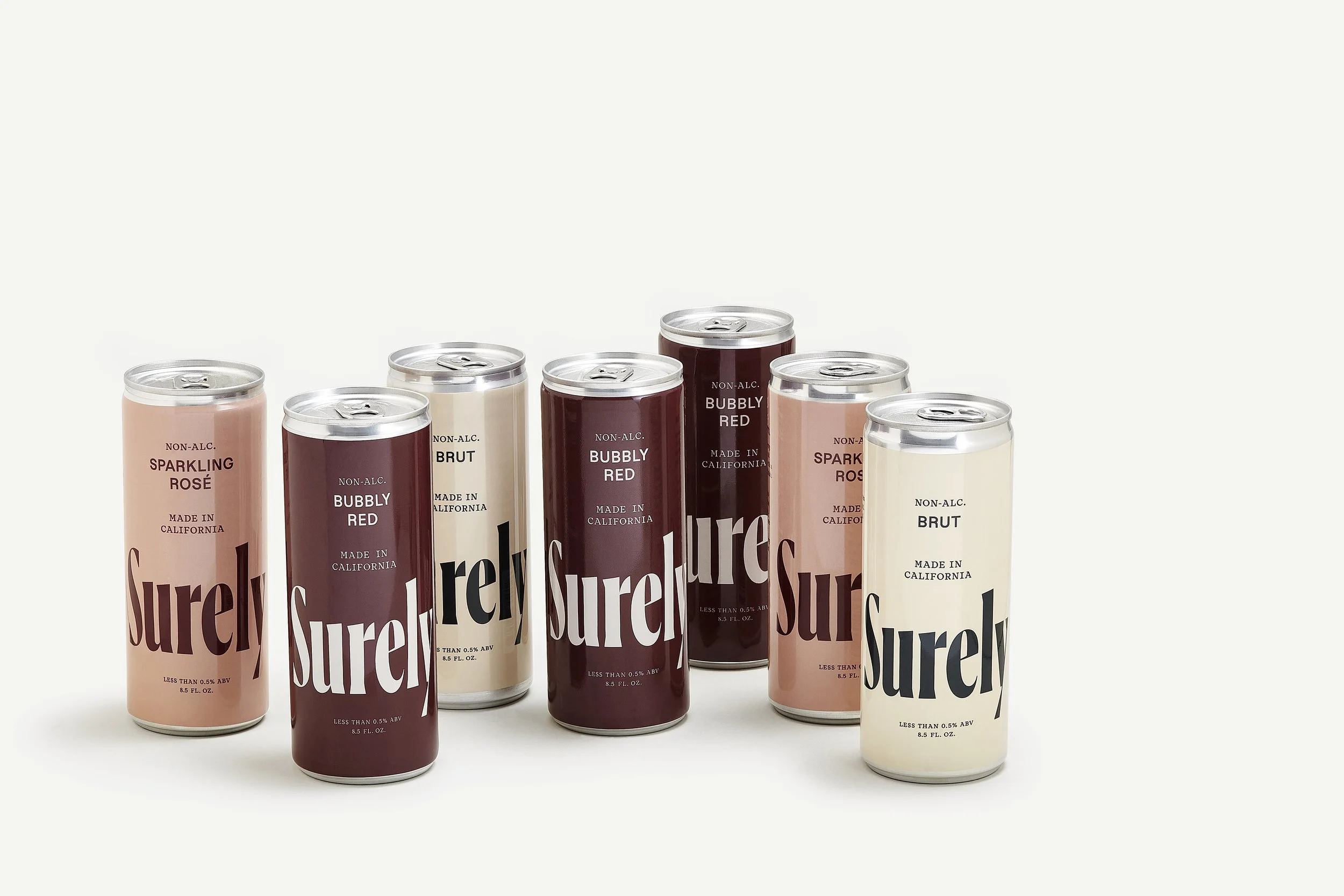 Six cans of Surely sparkling wine in different flavors with minimalist design, light background, and branding prominently displayed.