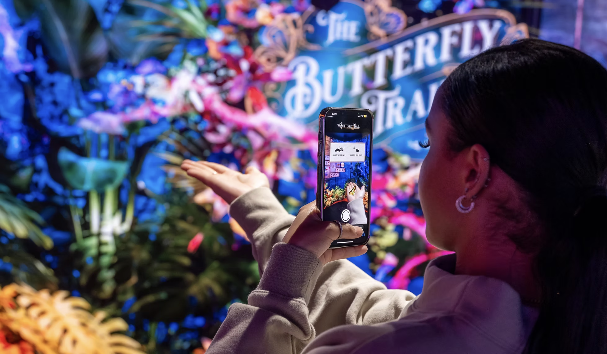 A woman taking a photo of a colorful floral display with her smartphone at Butterfly & Flower exhibit.