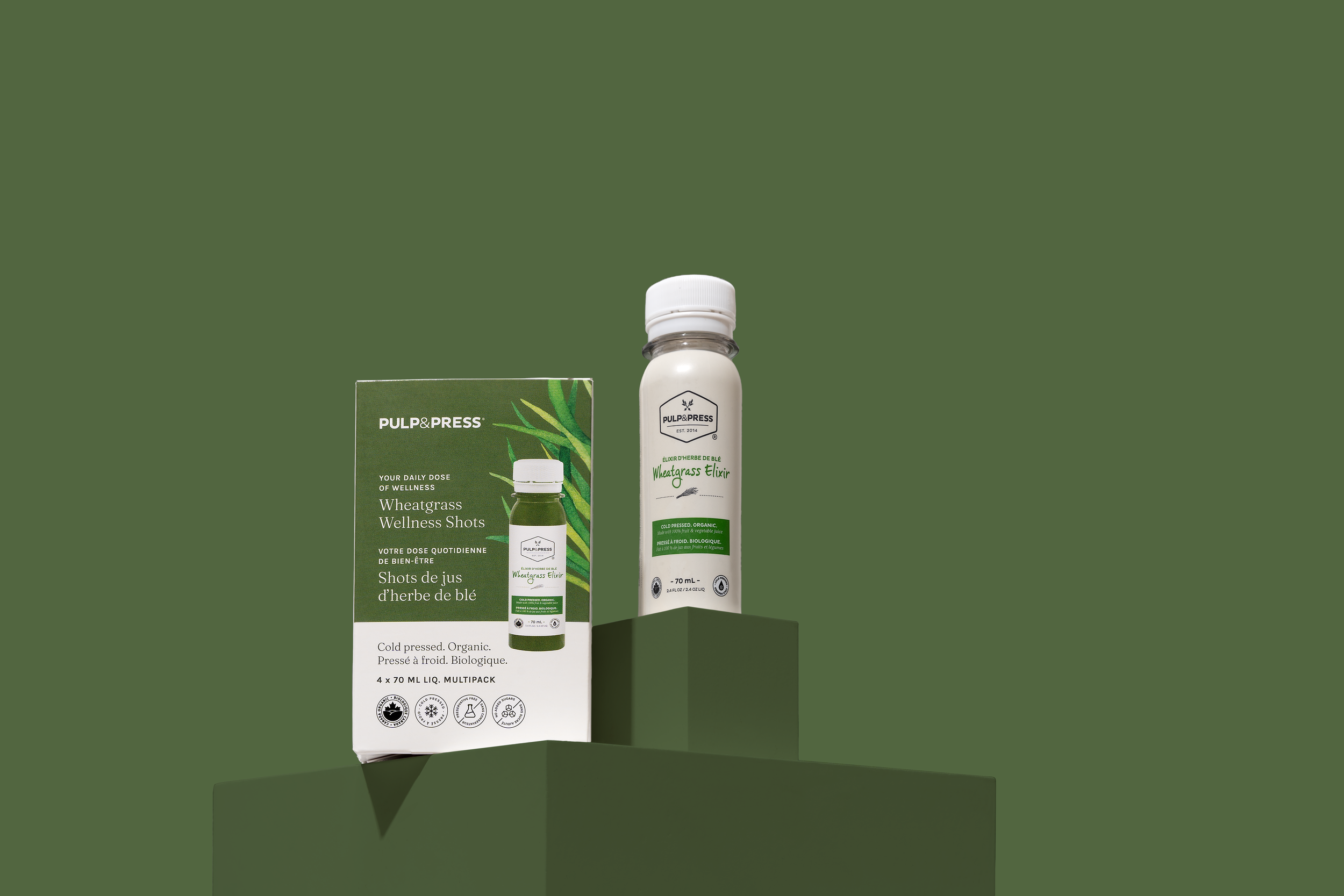 Package and bottle of Wheatgrass Wellness Shots from Pulp & Press on green pedestals against a green background.