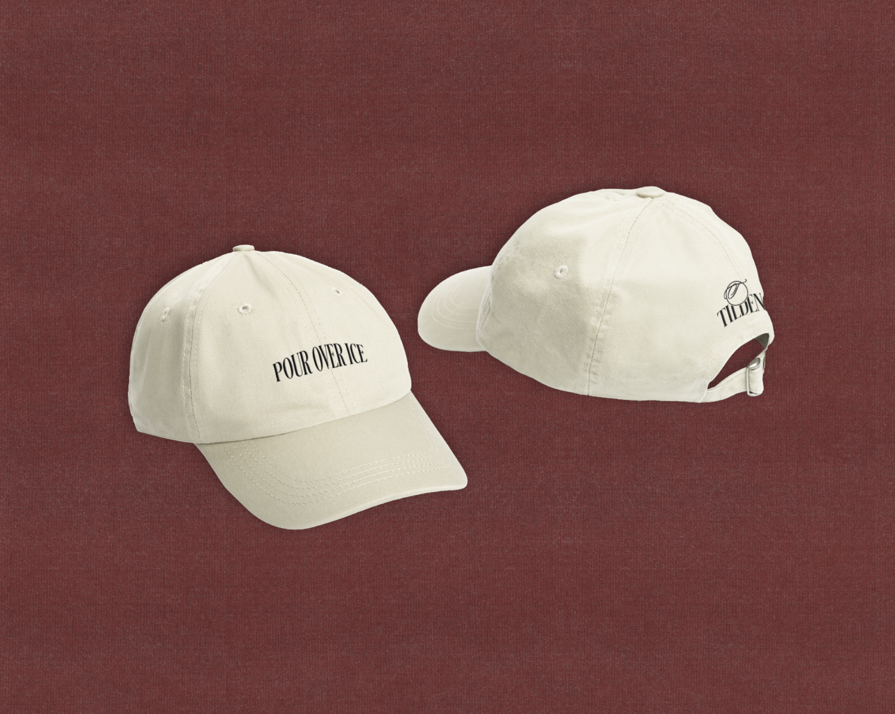 Two beige baseball caps on a red textured surface, one with 'POUR OVER ICE' text on the front and the other with 'TILEEN' logo on the back.