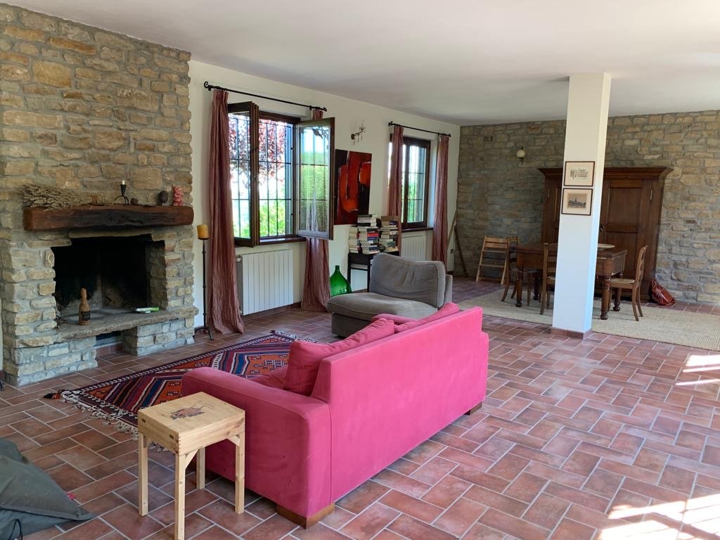 Living room with a brick fireplace, pink and gray couches, wooden side table, and a window with pink curtains.