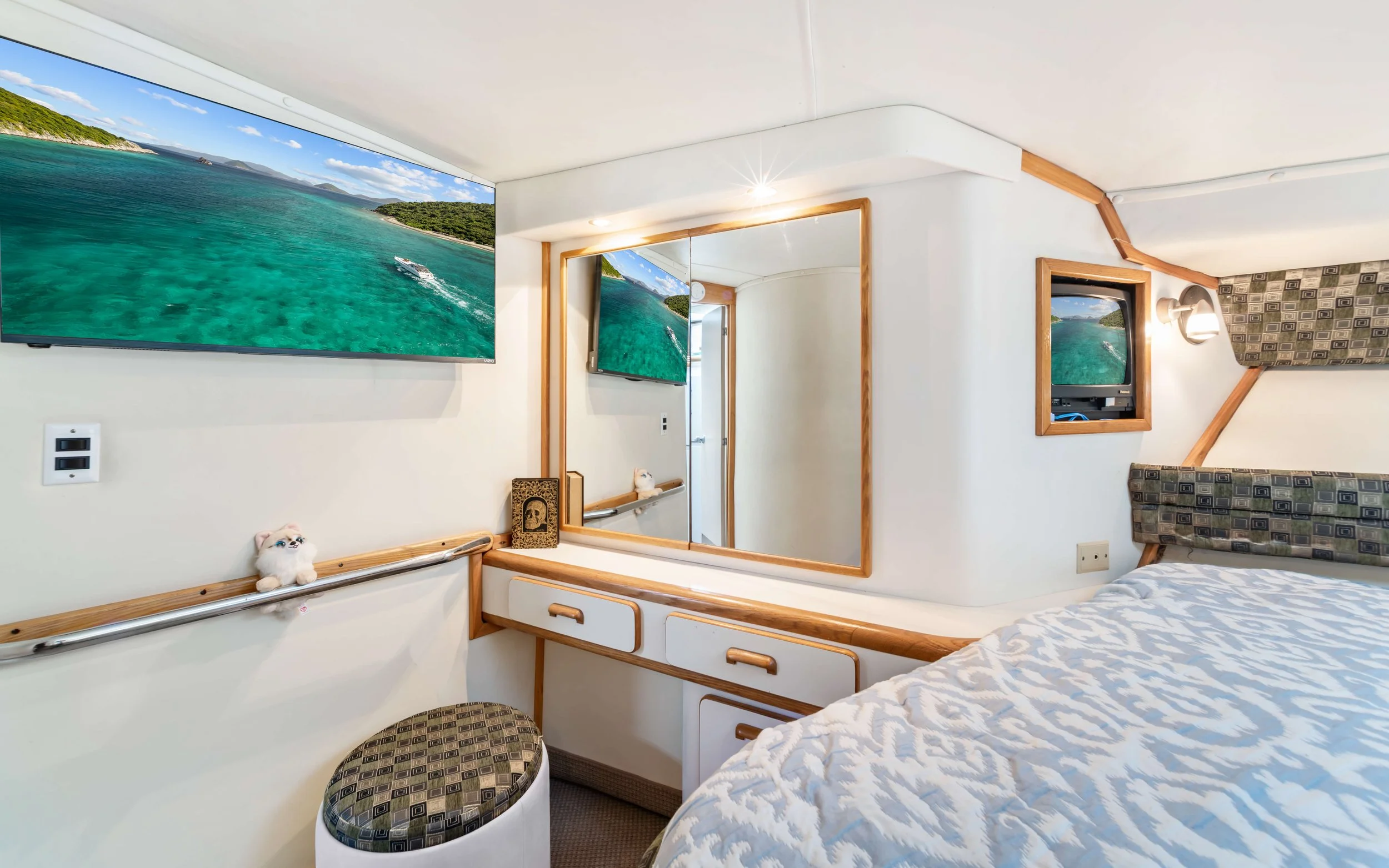 A bedroom with a bed, mirrors, and two wall-mounted televisions displaying a tropical ocean view.