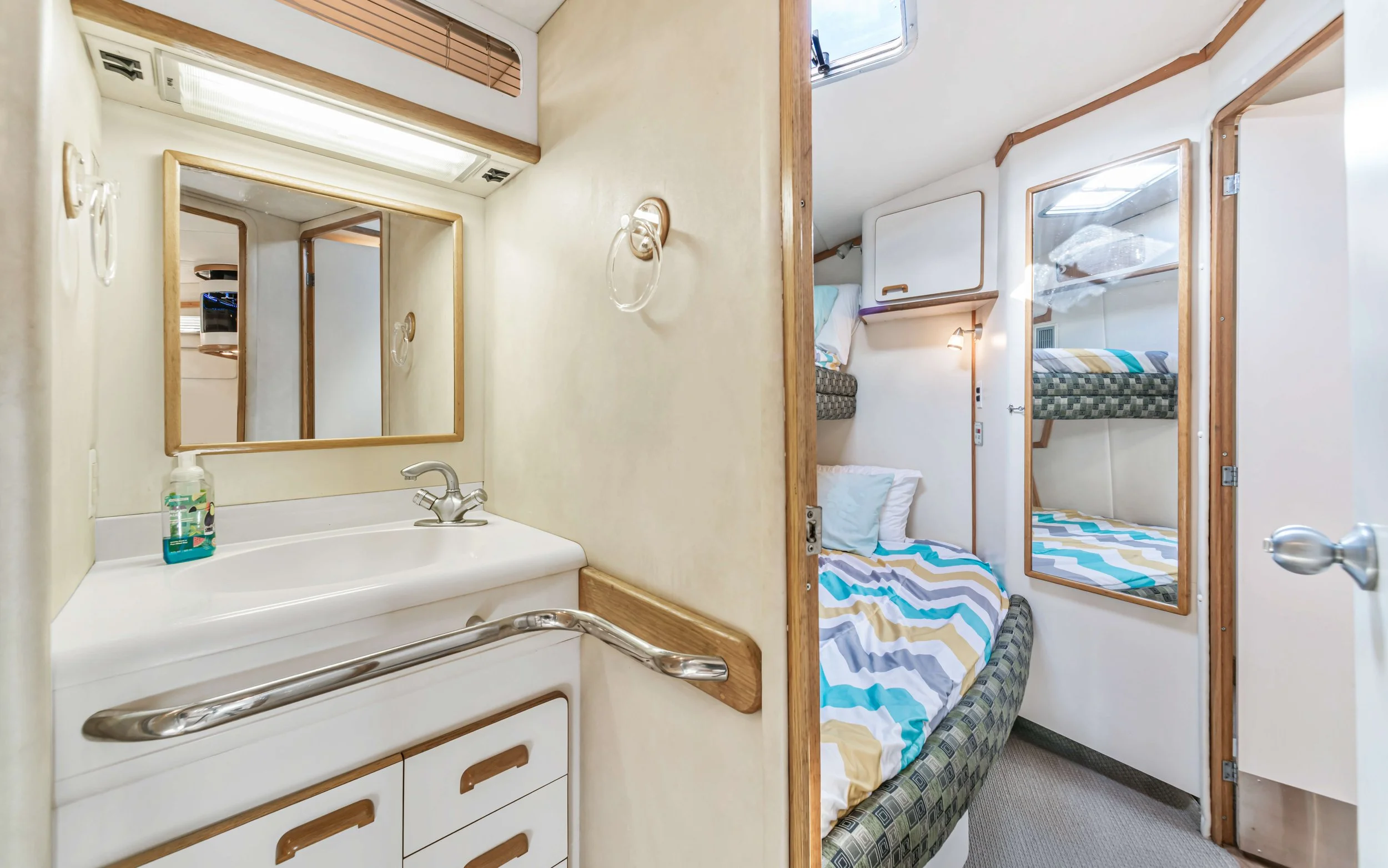 A small bathroom and a sleeping area with bunk beds, with a mirror and handrail in the bathroom, and beds with colorful striped bedding in the sleeping area.