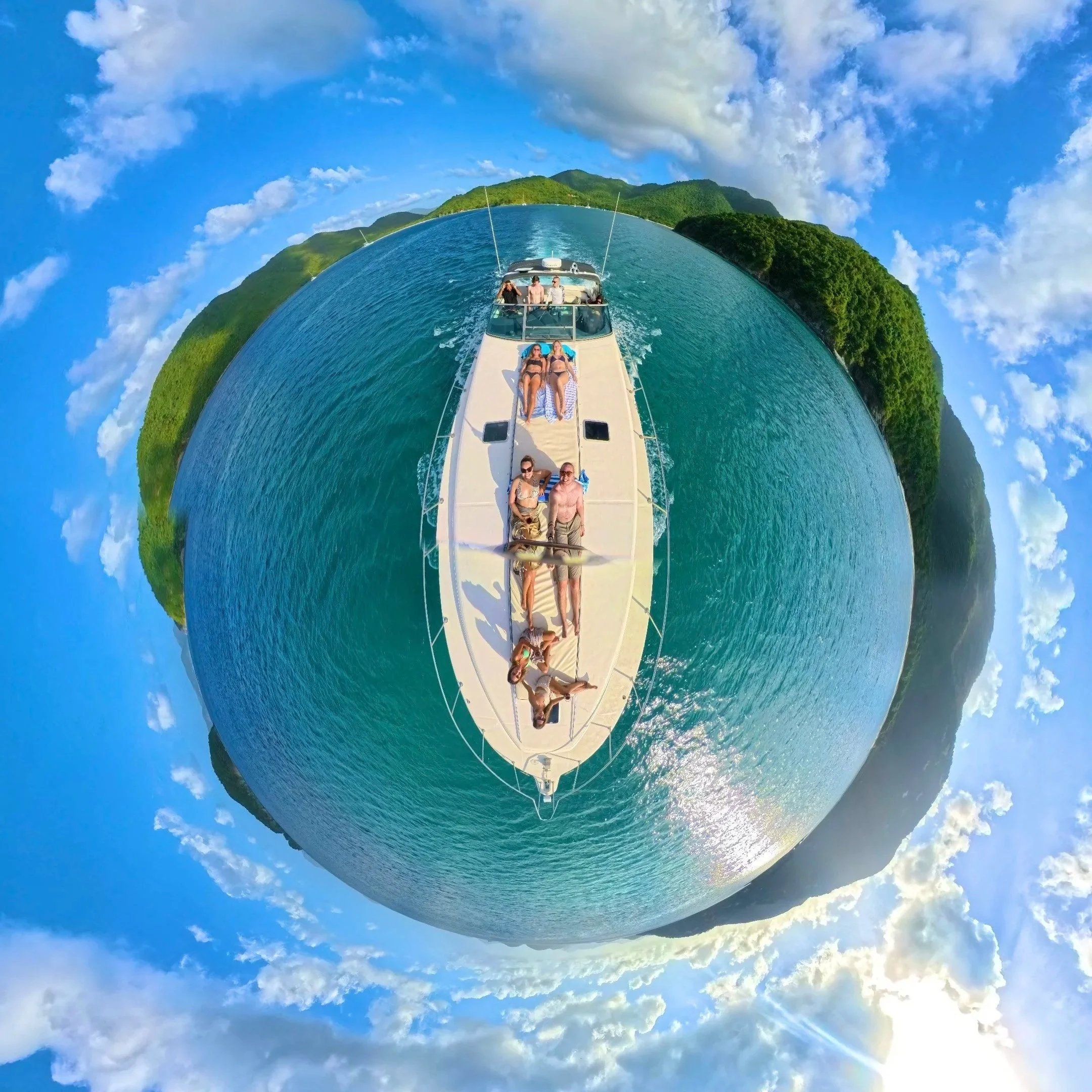 A group of people relaxing on a yacht in a tropical location, with lush green islands and blue sky surrounding a small circular view.
