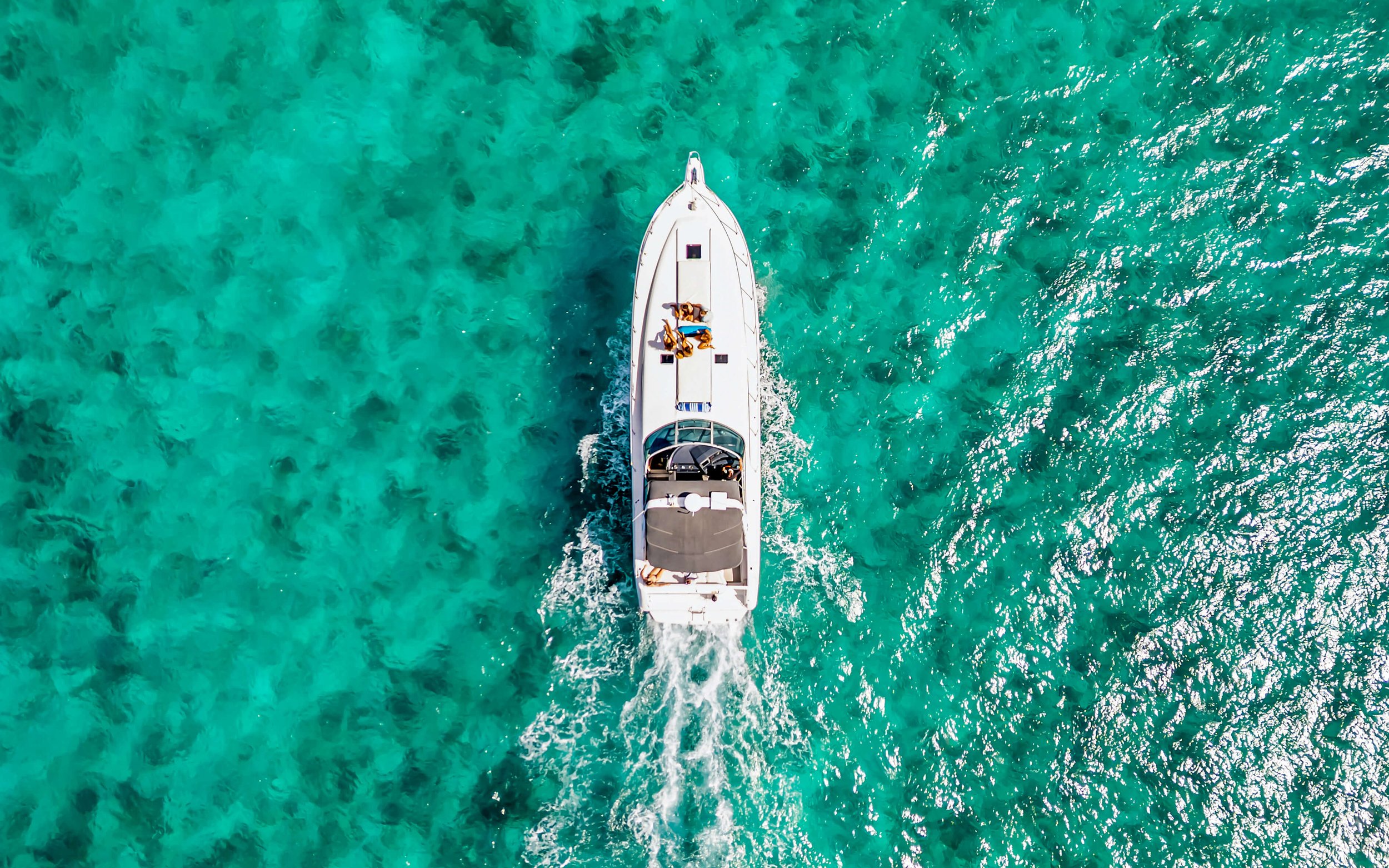 An aerial view of a white boat sailing on clear turquoise water.