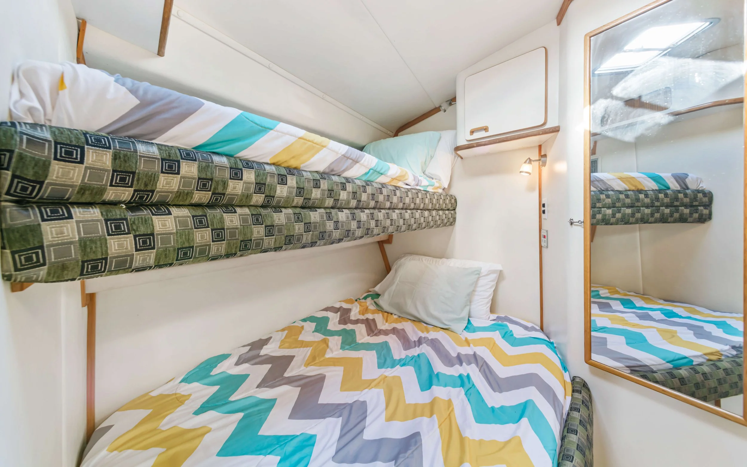 Small bedroom with bunk beds, colorful zigzag patterned bedding, white walls, wooden accents, mirror, and a small wall-mounted light.