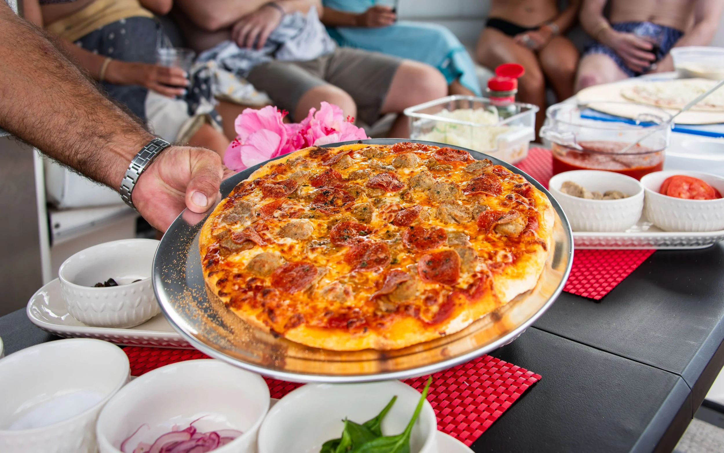Person serving a pizza at a gathering with people in the background.