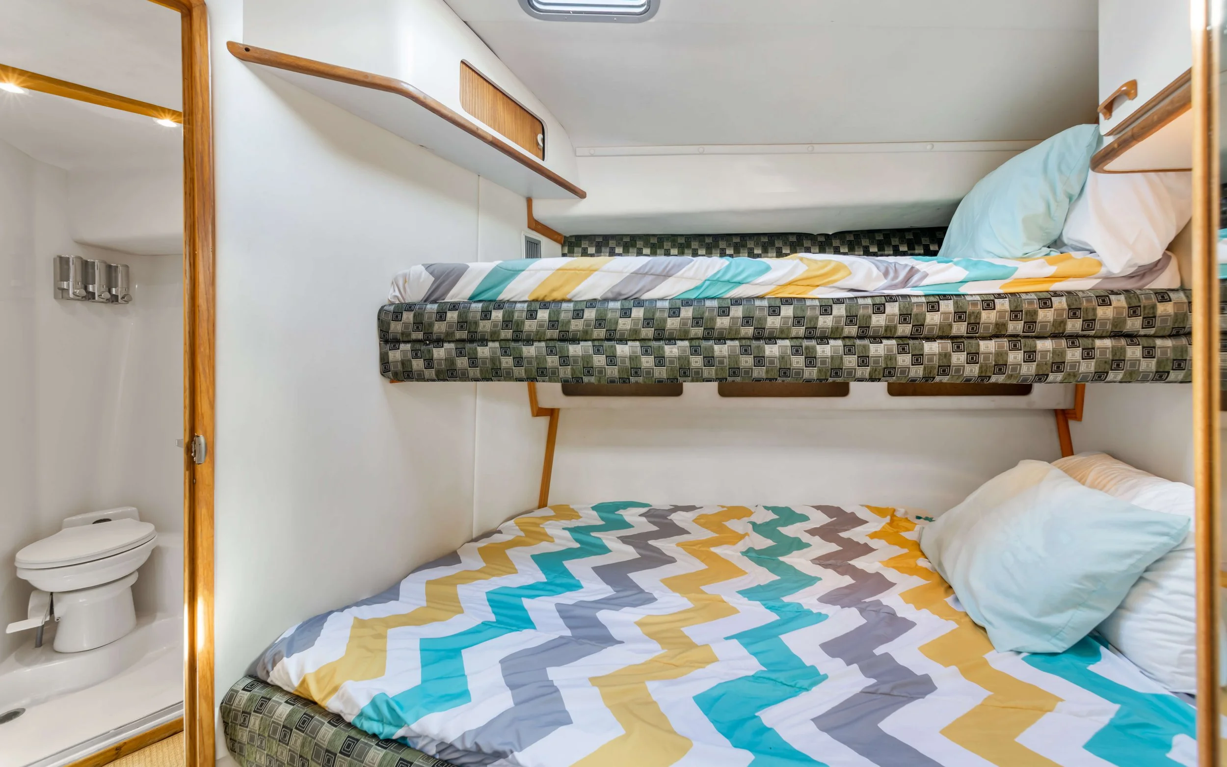 Bunk beds with colorful zigzag patterned bedding in a compact room, with a small bathroom visible in the corner.