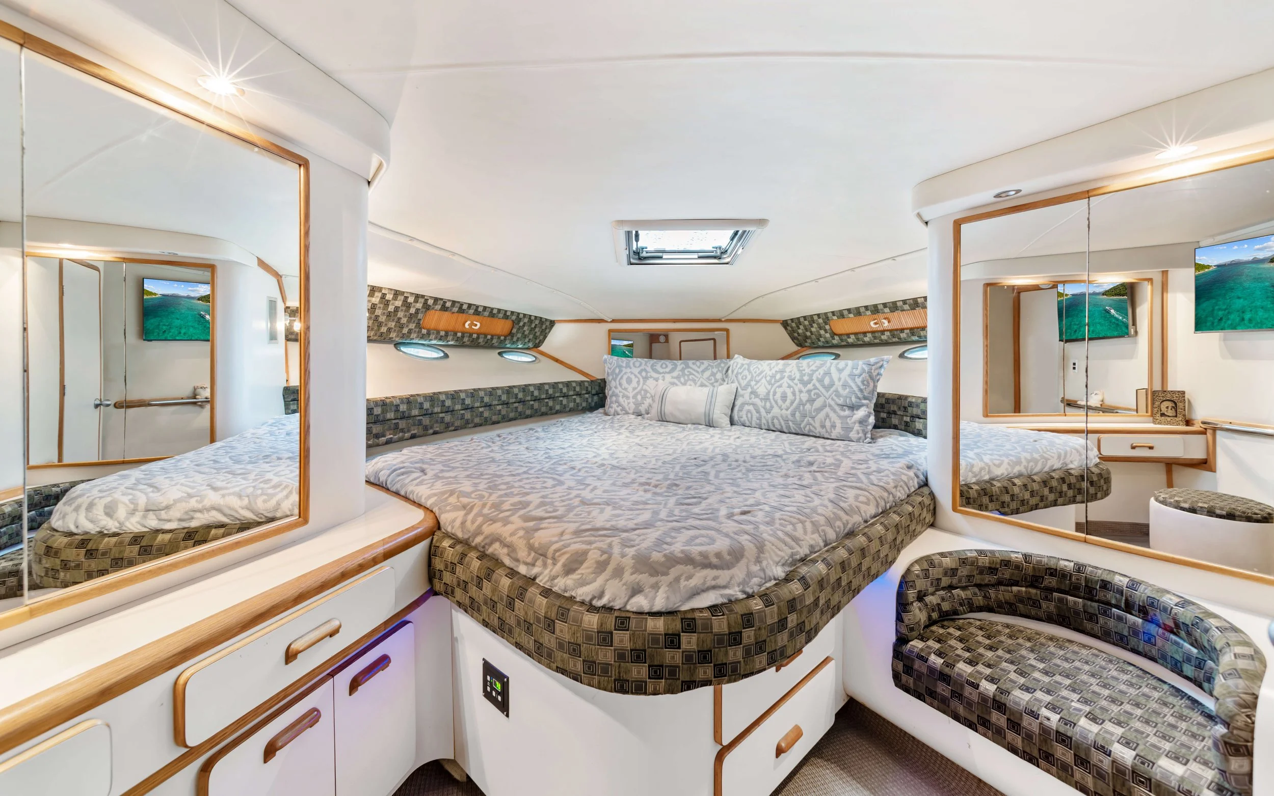 Compact boat cabin with a bed, monitors, mirrors, and built-in seating.