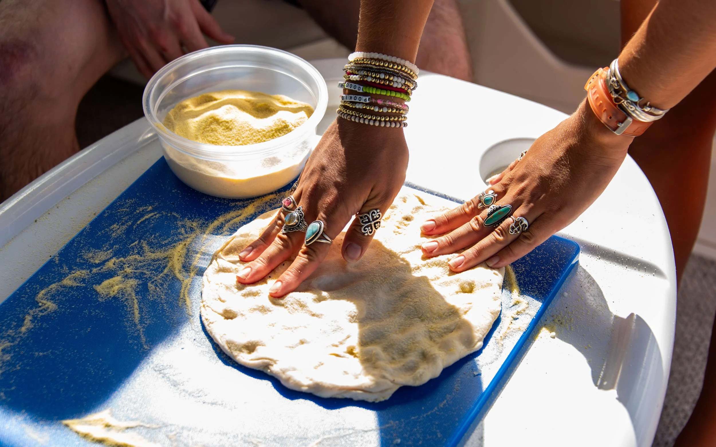 People pressing dough flat with their hands on a blue mat, with a bowl of flour nearby.