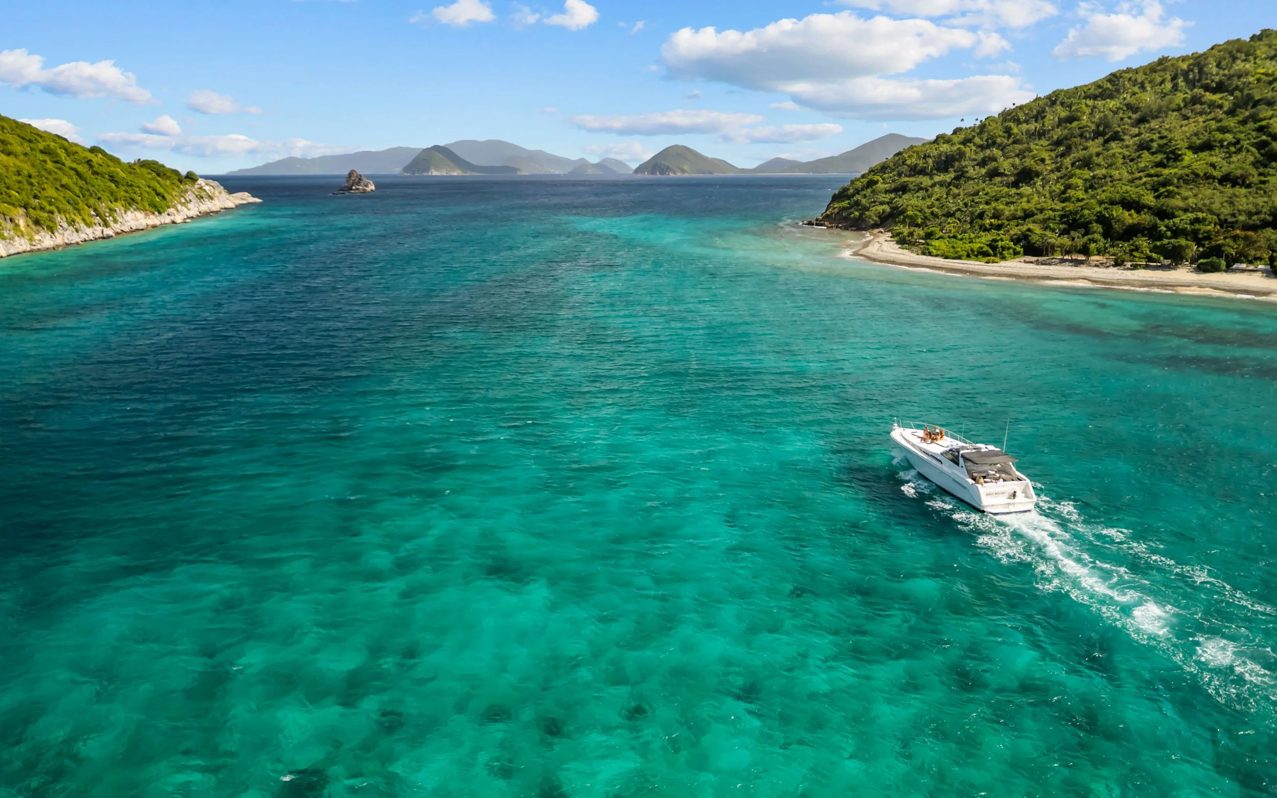 A white yacht sailing through clear turquoise waters between lush green islands under a partly cloudy sky.