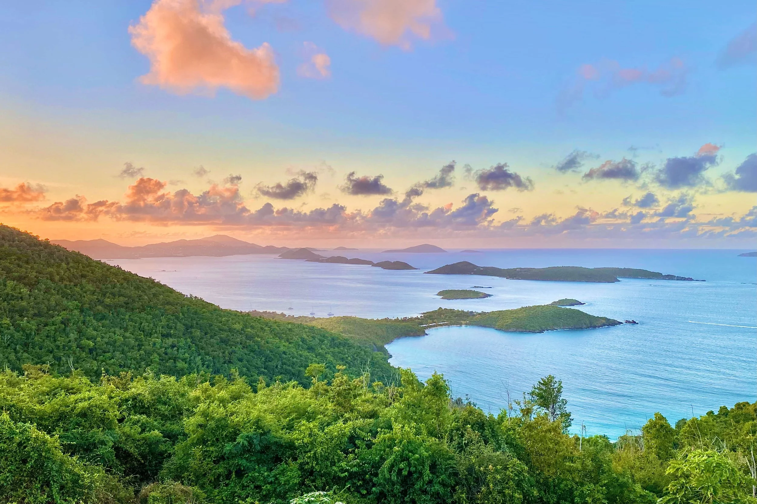 Scenic view of lush green islands and water during sunset with colorful clouds in the sky.