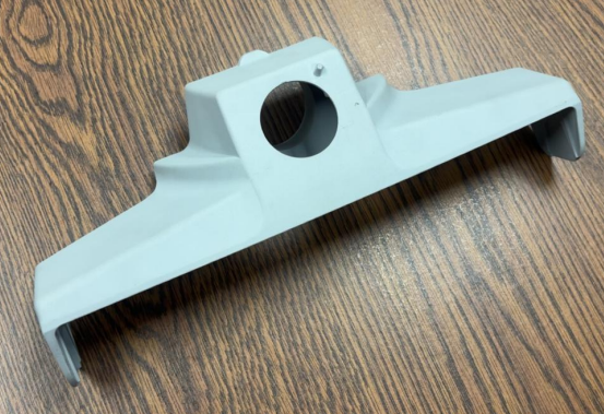 A gray plastic or metal bracket with a large circular hole in the center, resting on a wooden surface.