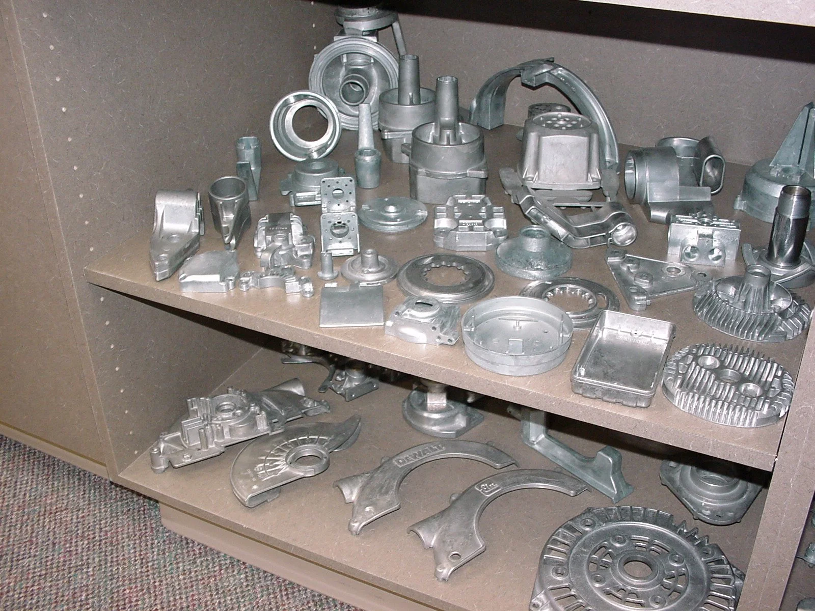 Metal engine parts and components on a two-tiered shelf in a workshop or storage area.