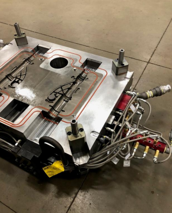 Close-up of a complex, metallic robotic or industrial component with various wires and tubing, on a concrete floor.