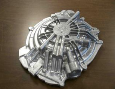 Silver metallic engine part with multiple cylindrical and tube-like structures on a wooden surface.