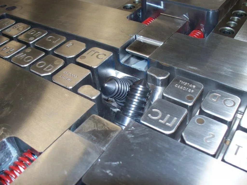 Close-up view of a metallic mechanical device with various labeled metal blocks and red coil springs.