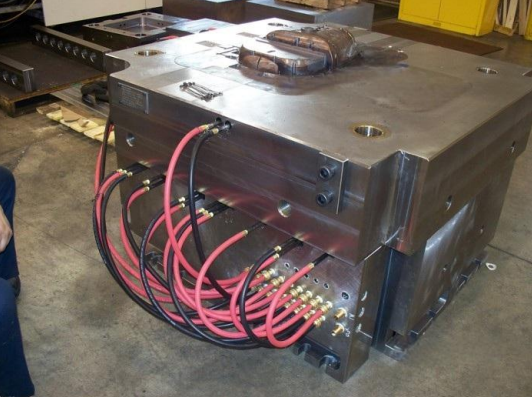 Large industrial metal machine with multiple pink cables connected at the front, located in a warehouse or workshop.