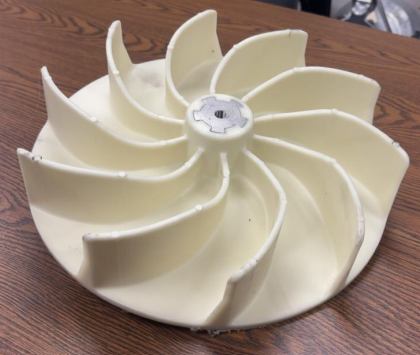 A white plastic fan impeller with multiple curved blades, resting on a wooden surface.
