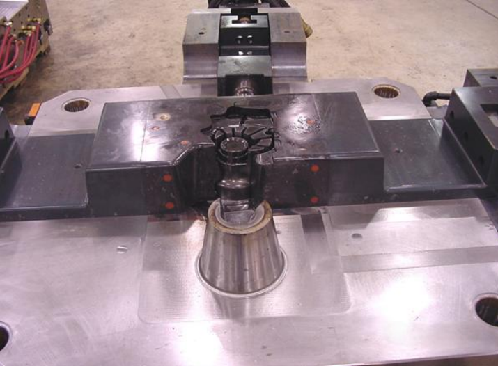 Close-up of a metal industrial mold or die with a captured metallic part at the center.