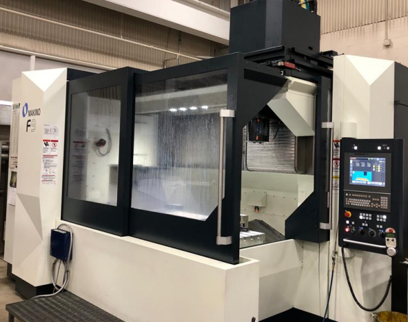 A large CNC machining center with a control panel on the right, enclosed in a transparent safety cover, located in an industrial setting.