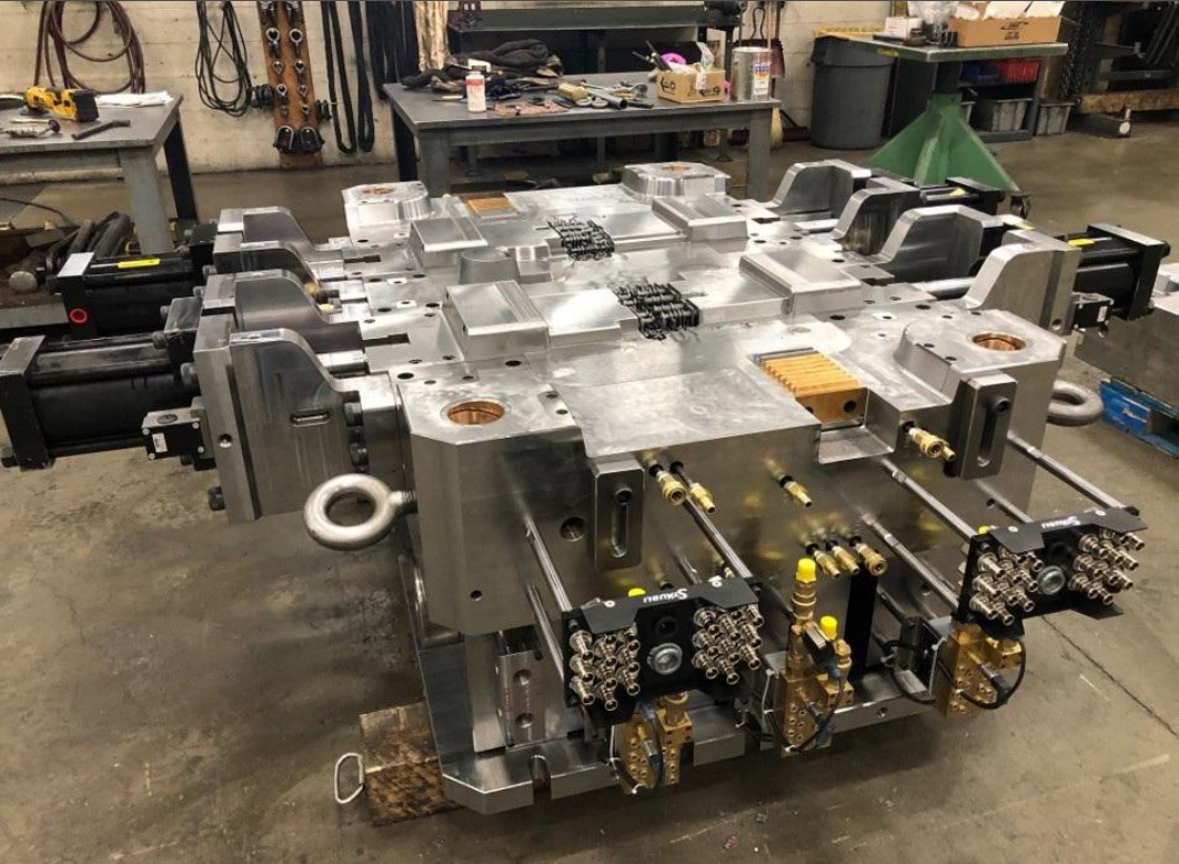 A large, industrial metal mold with multiple compartments and precision components, placed on a workbench in a workshop.