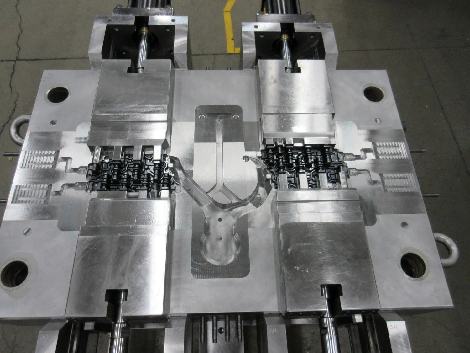A large, industrial metal mold with mechanical components, likely used for manufacturing or injection molding, set on a workshop floor with visible cracks.