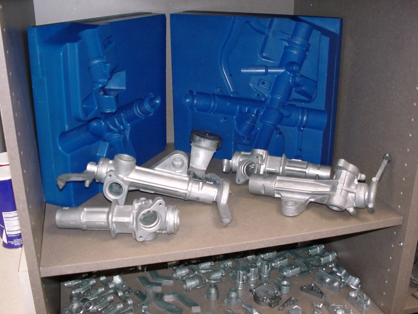 Metal mechanical parts on a shelf with blue mounting boards in the background.