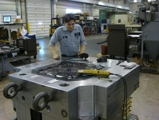 A man working on a large, industrial metal component in a manufacturing workshop.