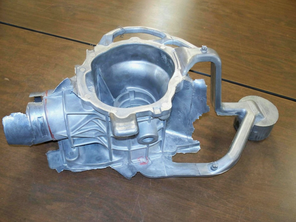 A metallic mechanical part, likely a component of an engine or machinery, placed on a wooden surface.