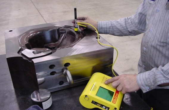 A person in a striped shirt using testing equipment on a metallic device, with a yellow testing device connected to the metallic device.