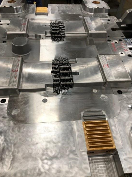 Close-up of a metallic industrial mold with multiple components and black mechanical parts inside.