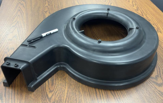 Large black plastic ring with a rectangular attachment, resting on a wooden table, with a white marker nearby.