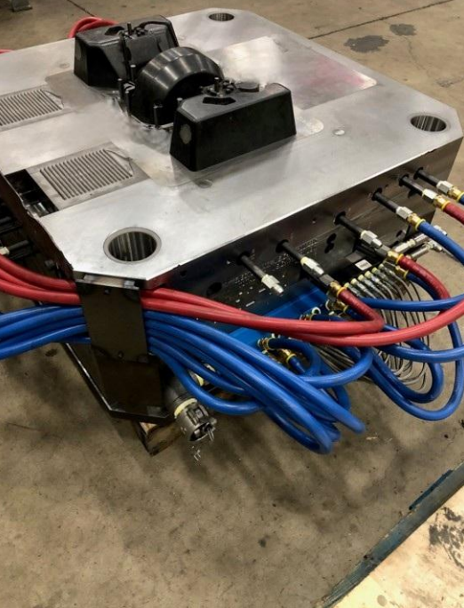 A large industrial electrical device with numerous red and blue cables connected, situated on a concrete floor in what appears to be a workshop or warehouse.