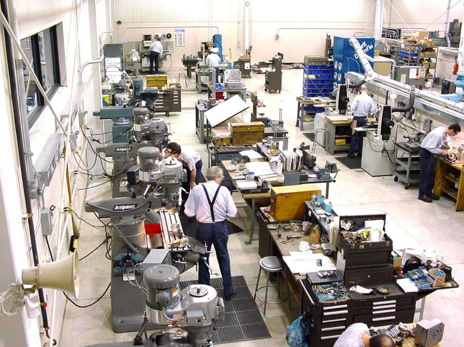Workers in a manufacturing or machining workshop working at various stations with machinery and tools.