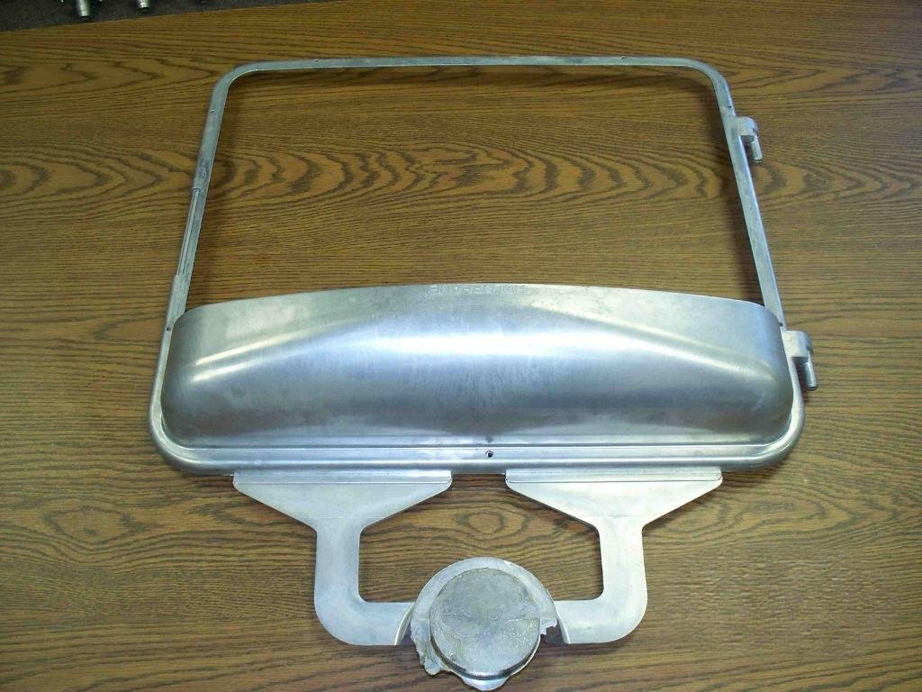 A metal heat lamp or cooker with a rounded cover and a support frame, placed on a wooden surface.